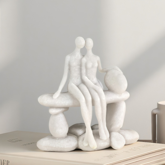 Бяла статуетка с каменен ефект, изобразяваща влюбена двойка, седяща прегърната на пейка
