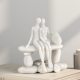 Бяла статуетка с каменен ефект, изобразяваща влюбена двойка, седяща прегърната на пейка